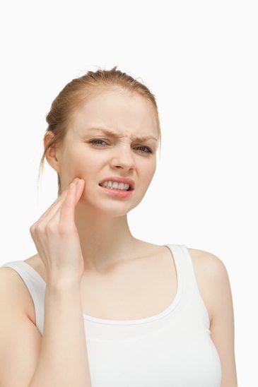 a woman clutches the side of her face to quell a wisdom tooth infection